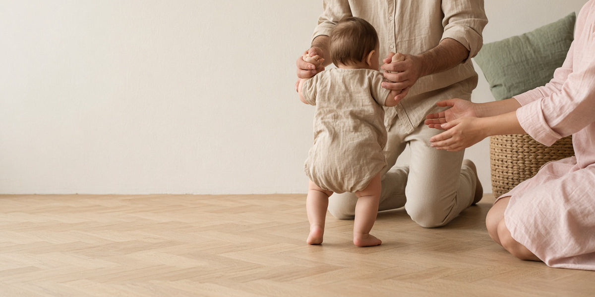 Parents accompagnant les premiers pas de leur bébé sur un parquet clair.